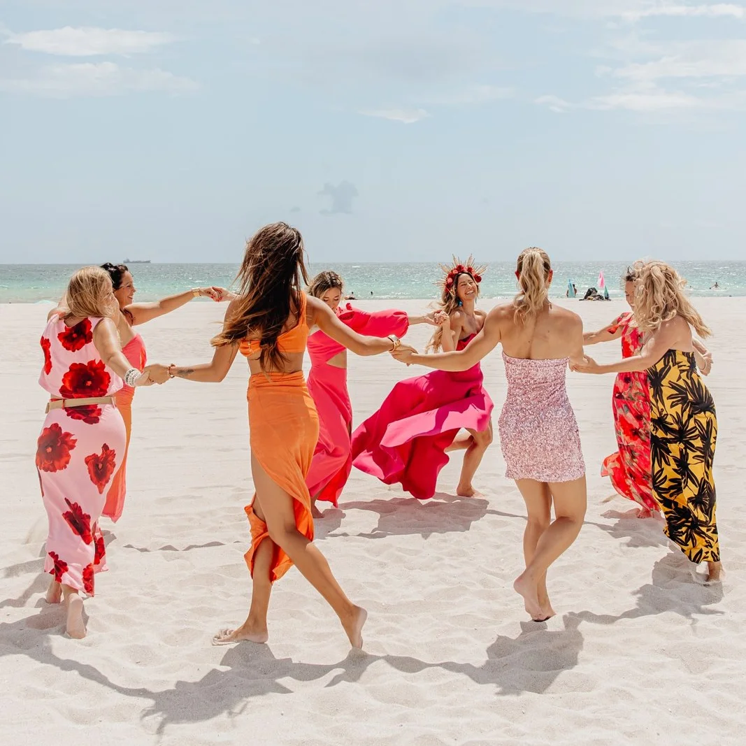 The Summit women holding hands in a circle on the sand, the ocean behind them