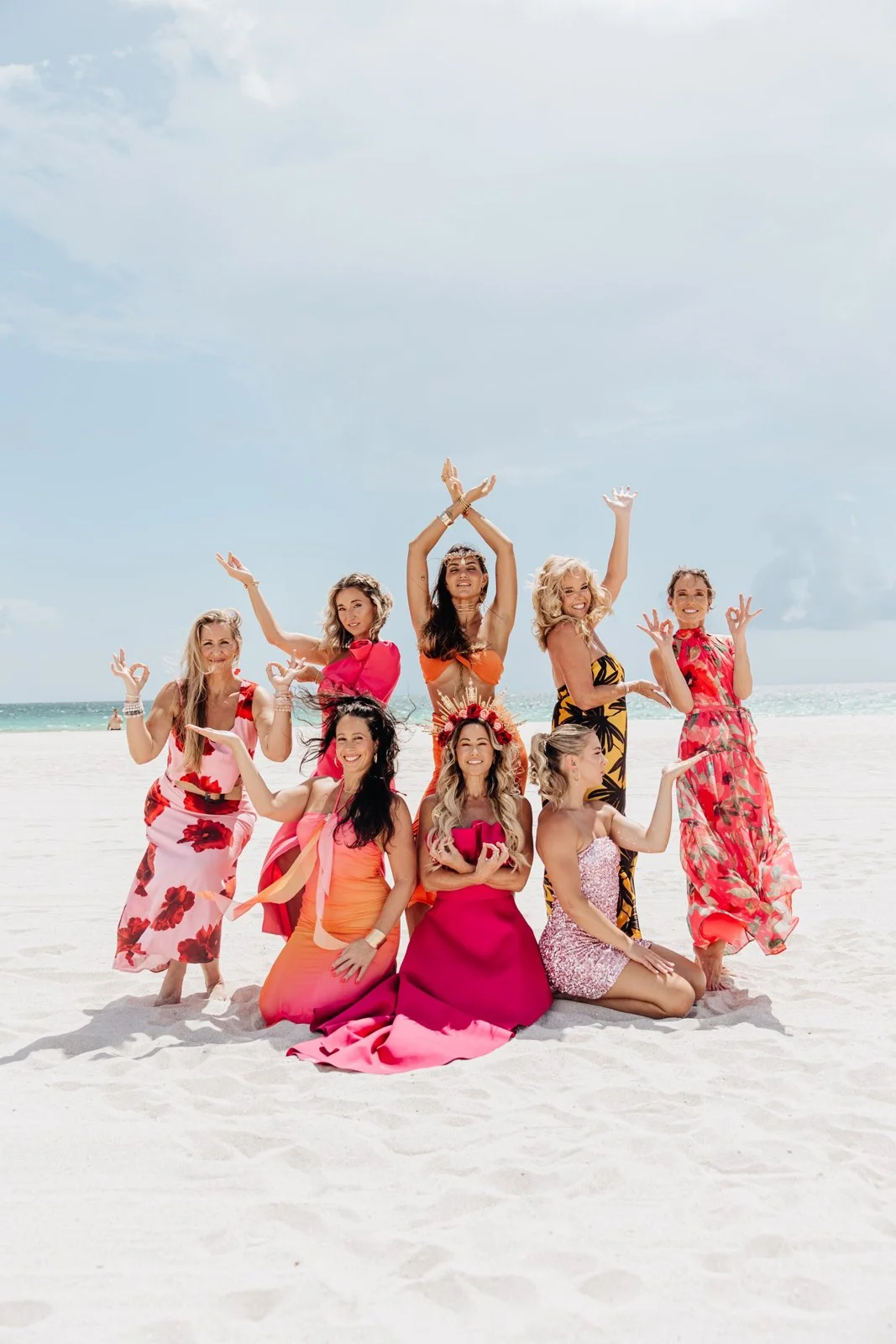 Women in pink and orange gowns gathered close on the sand