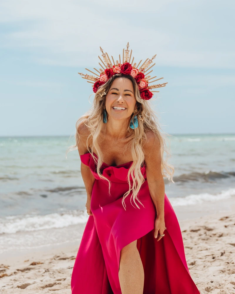 Vanessa Lambert laughing on the beach in a flower crown and red gown