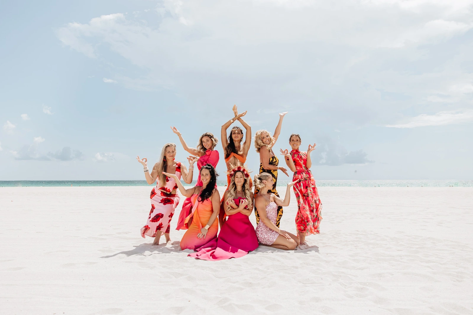 Eight women posing together on the beach, arms raised